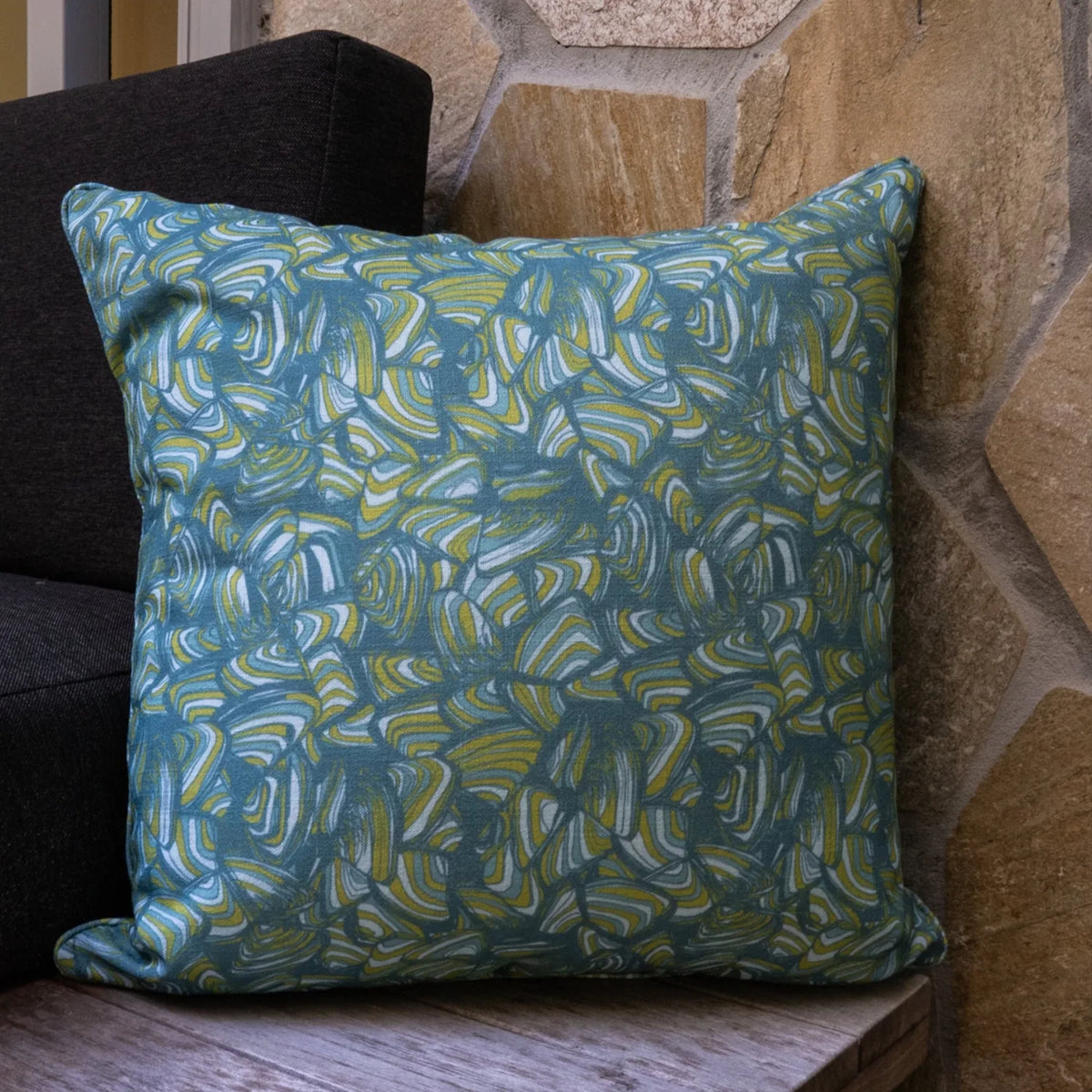 Square Mangrove Pipi cushion with blue, green and white abstract print styled against a stone wall.