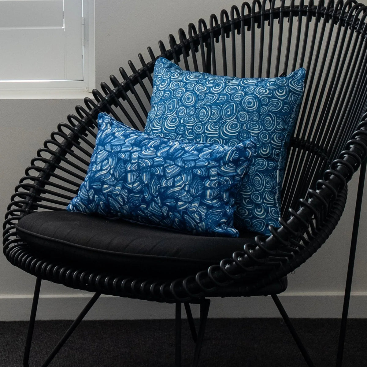 Pacific cushions styled on a black woven chair with a square Growth Rings cushion and a Pipi lumbar cushion.