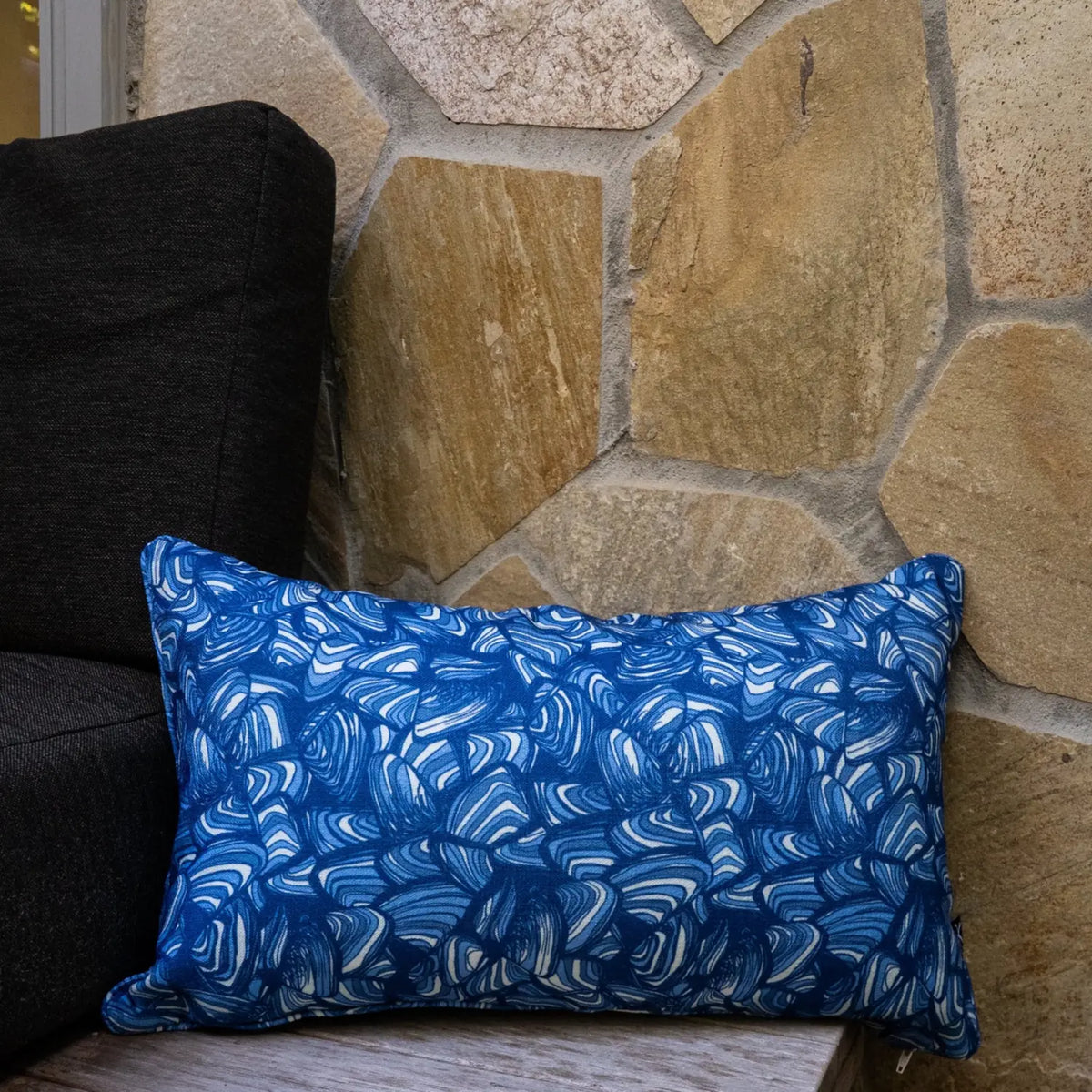 Pacific Pipi lumbar cushion in blue and white abstract print styled against a stone wall.
