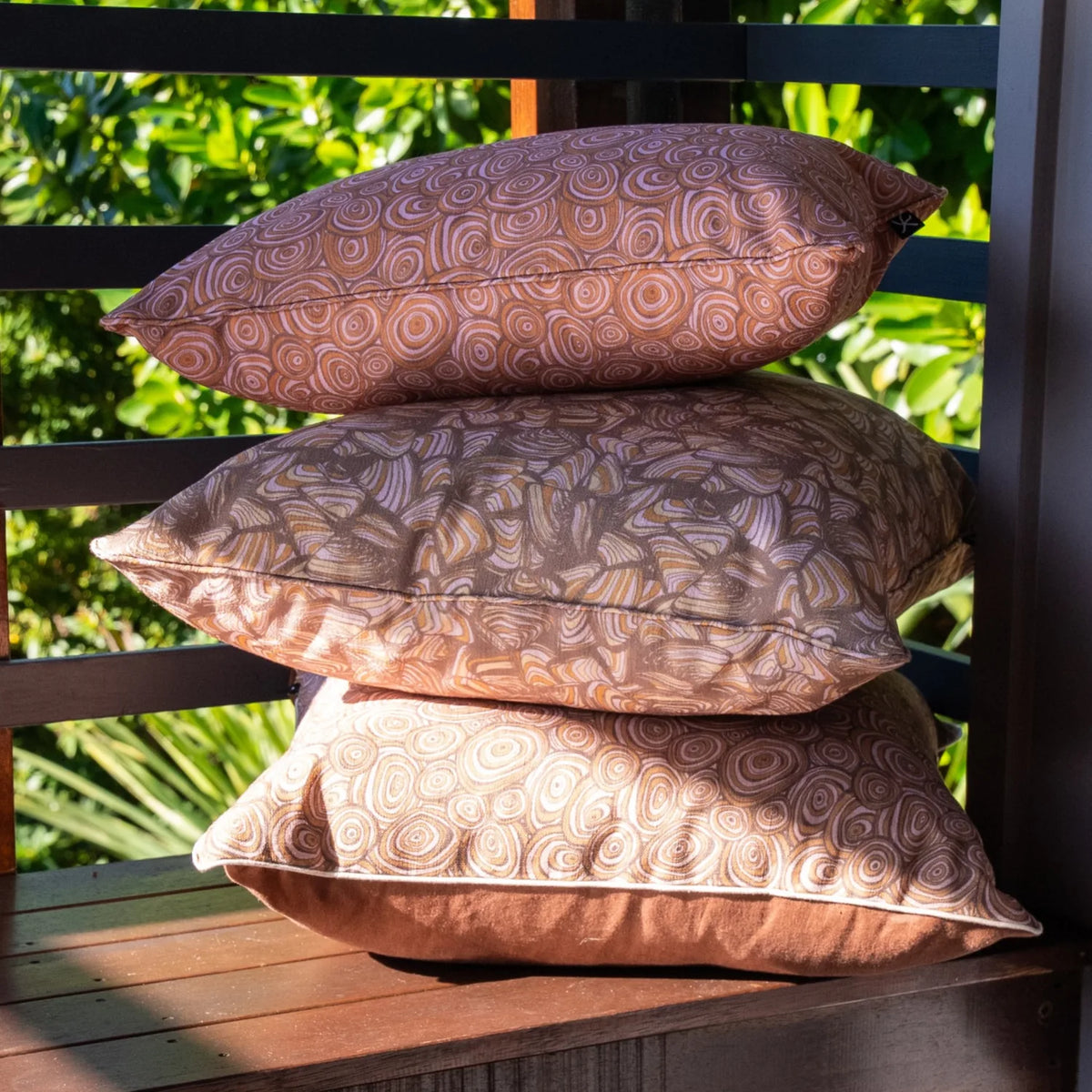 Outdoor indoor cushion covers in the Claytons colourway, including Growth Rings and Pipi prints, stacked on an outdoor bench.