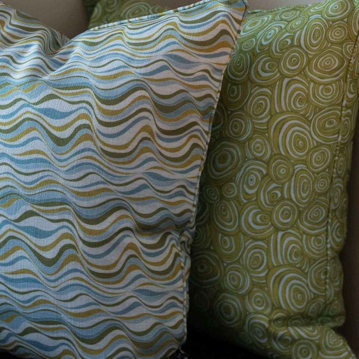 Close-up of Outdoor Indoor Growth Rings cushion cover in Mangrove beside a wave print cushion cover