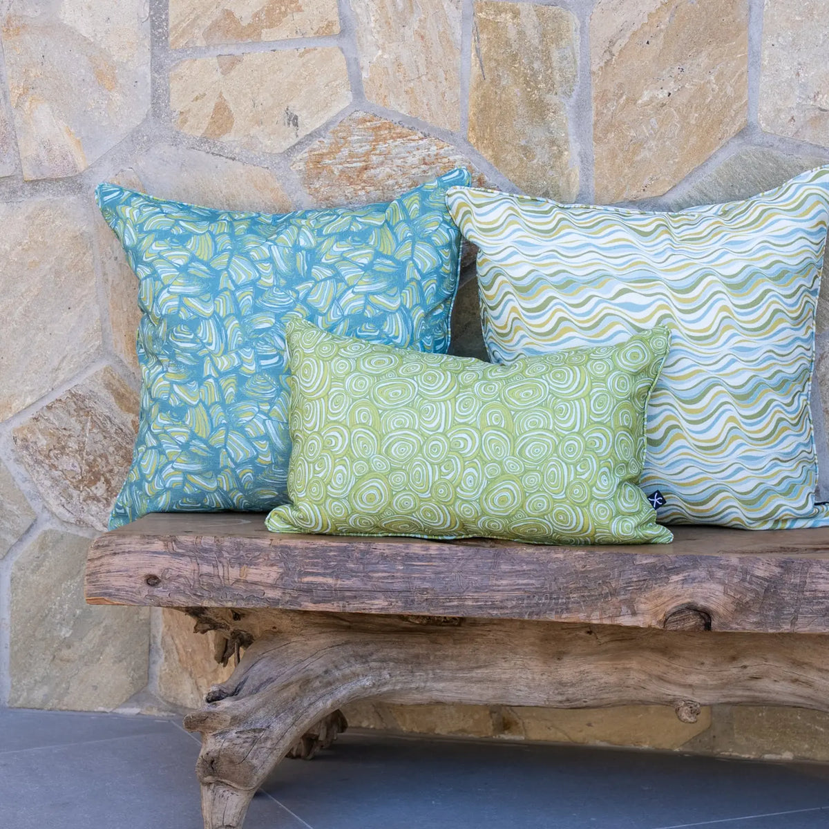 Outdoor Indoor Growth Rings cushion cover in Mangrove lumbar cushion with wave print and teal swirl print cushions on a stone wall bench