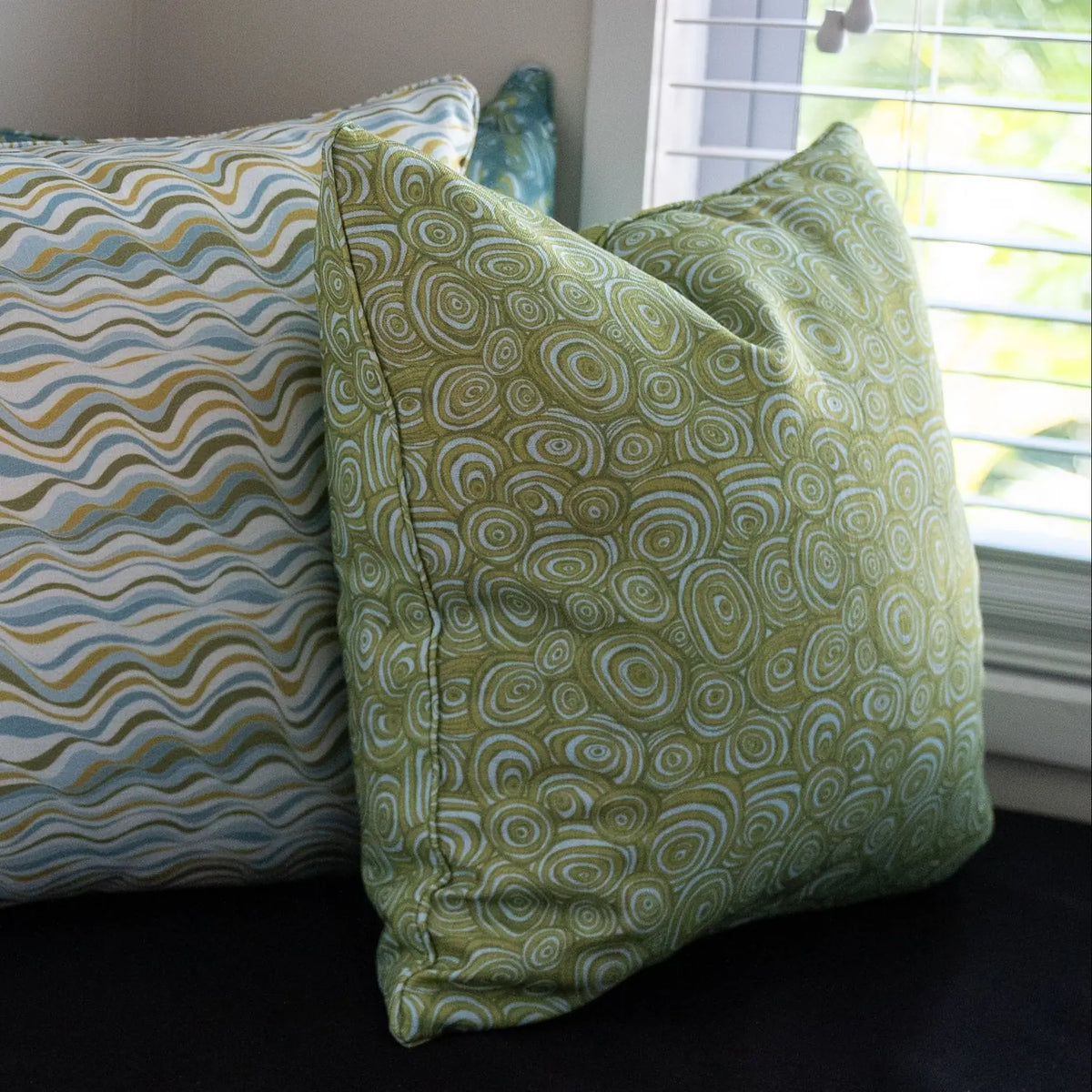 Outdoor Indoor Growth Rings cushion cover in Mangrove styled on a sunny window bench beside a wave print cushion