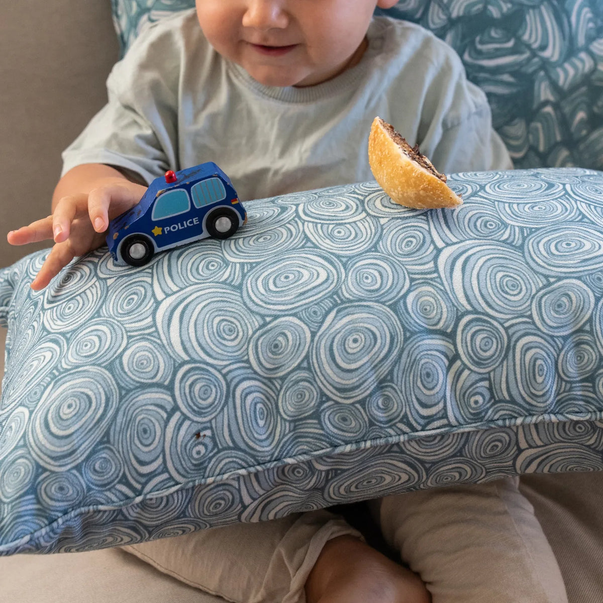 Close-up of the Outdoor Indoor Growth Rings cushion cover in Frenchman fabric, with a toddler's toy police car