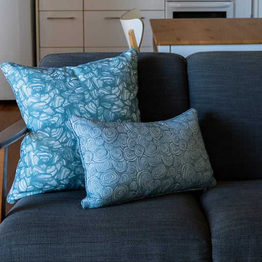 Outdoor Indoor Growth Rings cushion cover in Frenchman paired with a teal swirl print cushion on an indoor sofa, kitchen setting