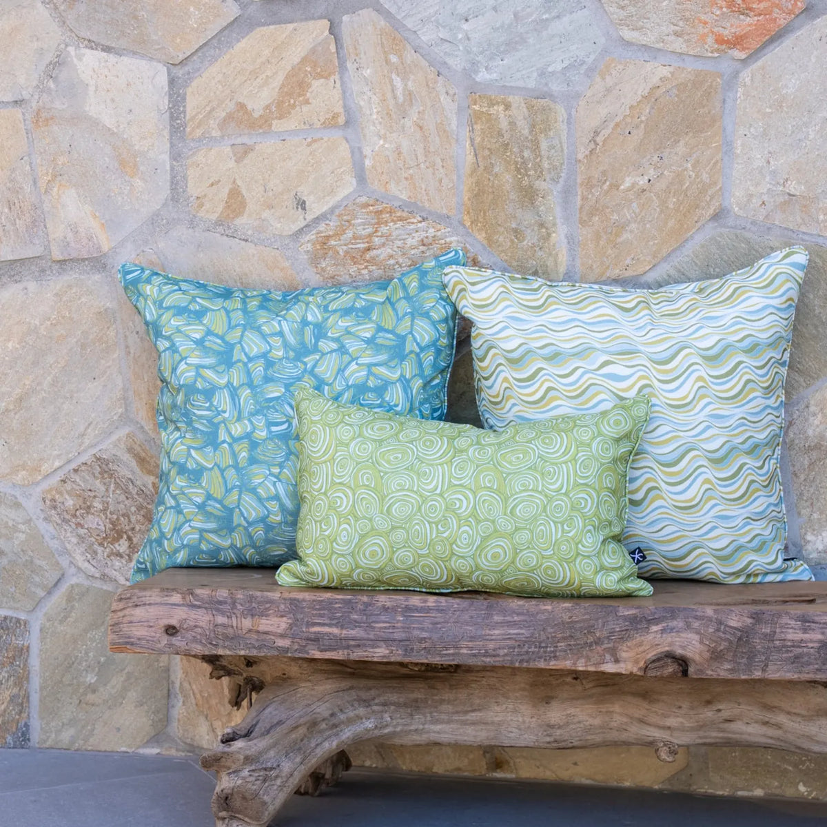 Mangrove colourway cushion covers featuring Straddie Stripe, Pipi and Growth Rings prints styled together on a timber bench.