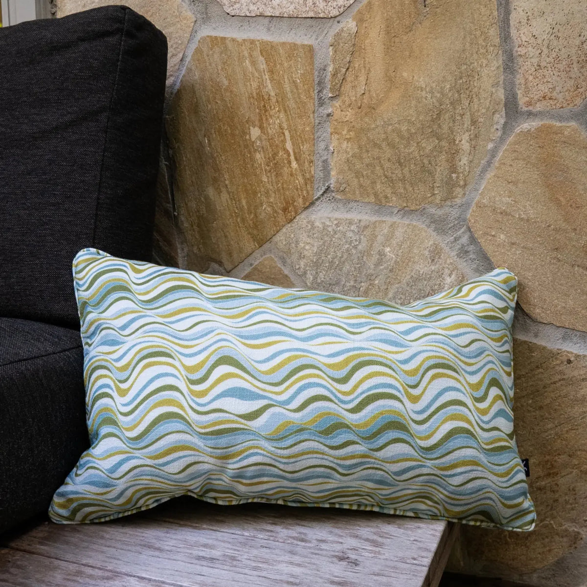 Mangrove Straddie Stripe outdoor indoor cushion cover in a rectangular lumbar size styled on an outdoor chair beside a stone wall.