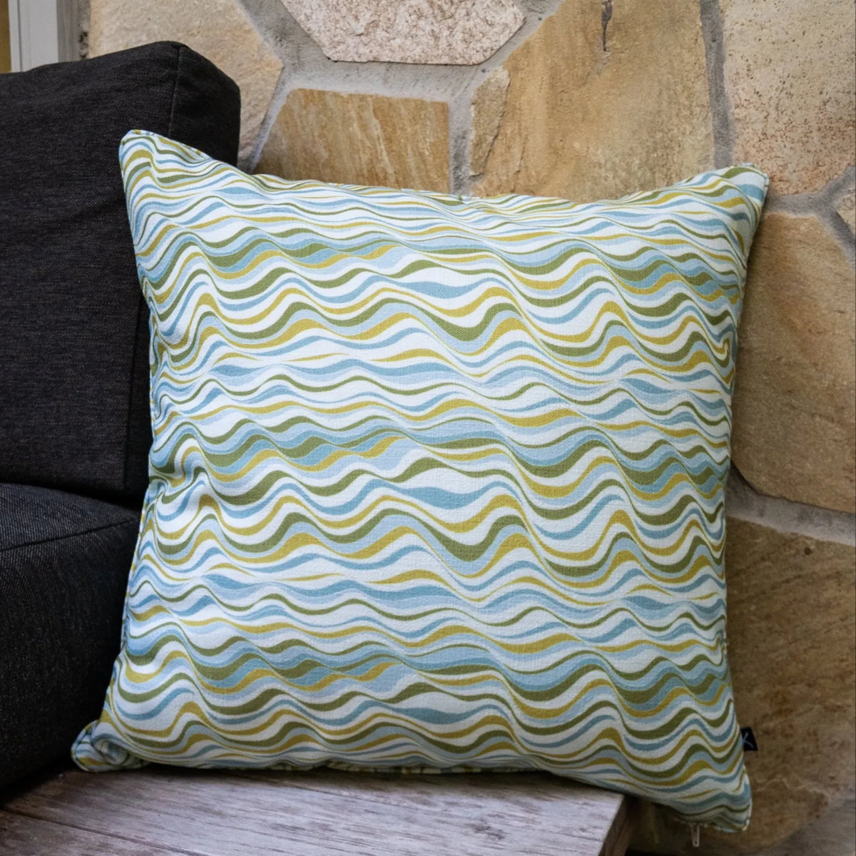 Mangrove Straddie Stripe outdoor indoor cushion cover in a square size styled on an outdoor chair beside a stone wall.