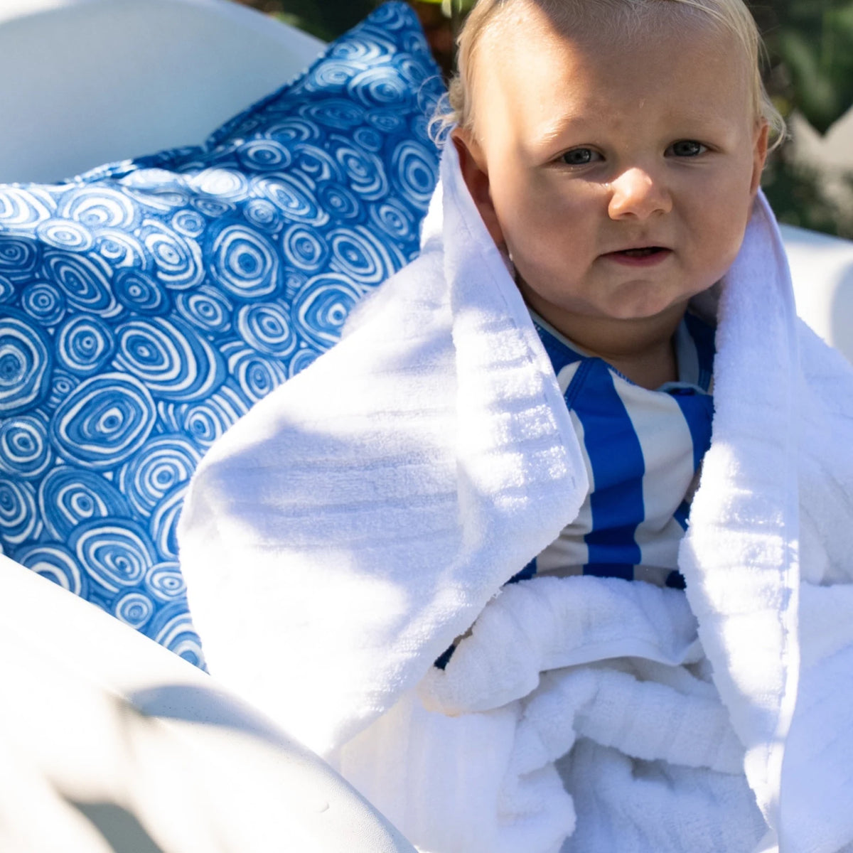Ocean Growth Rings outdoor indoor cushion cover in blue styled behind a baby wrapped in a white towel by the pool.