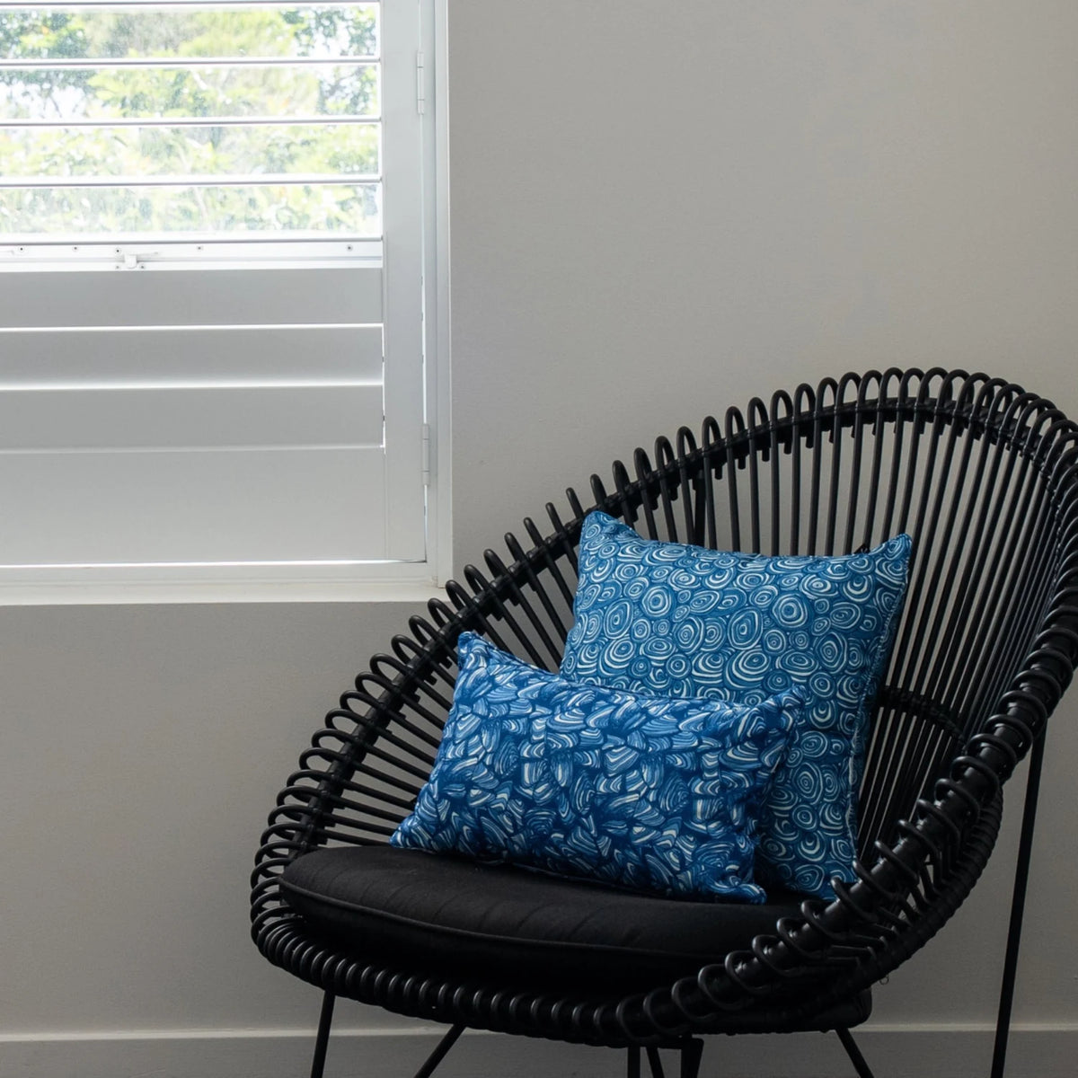 Ocean Growth Rings outdoor indoor cushion cover styled with a coordinating blue print cushion on a black woven chair.